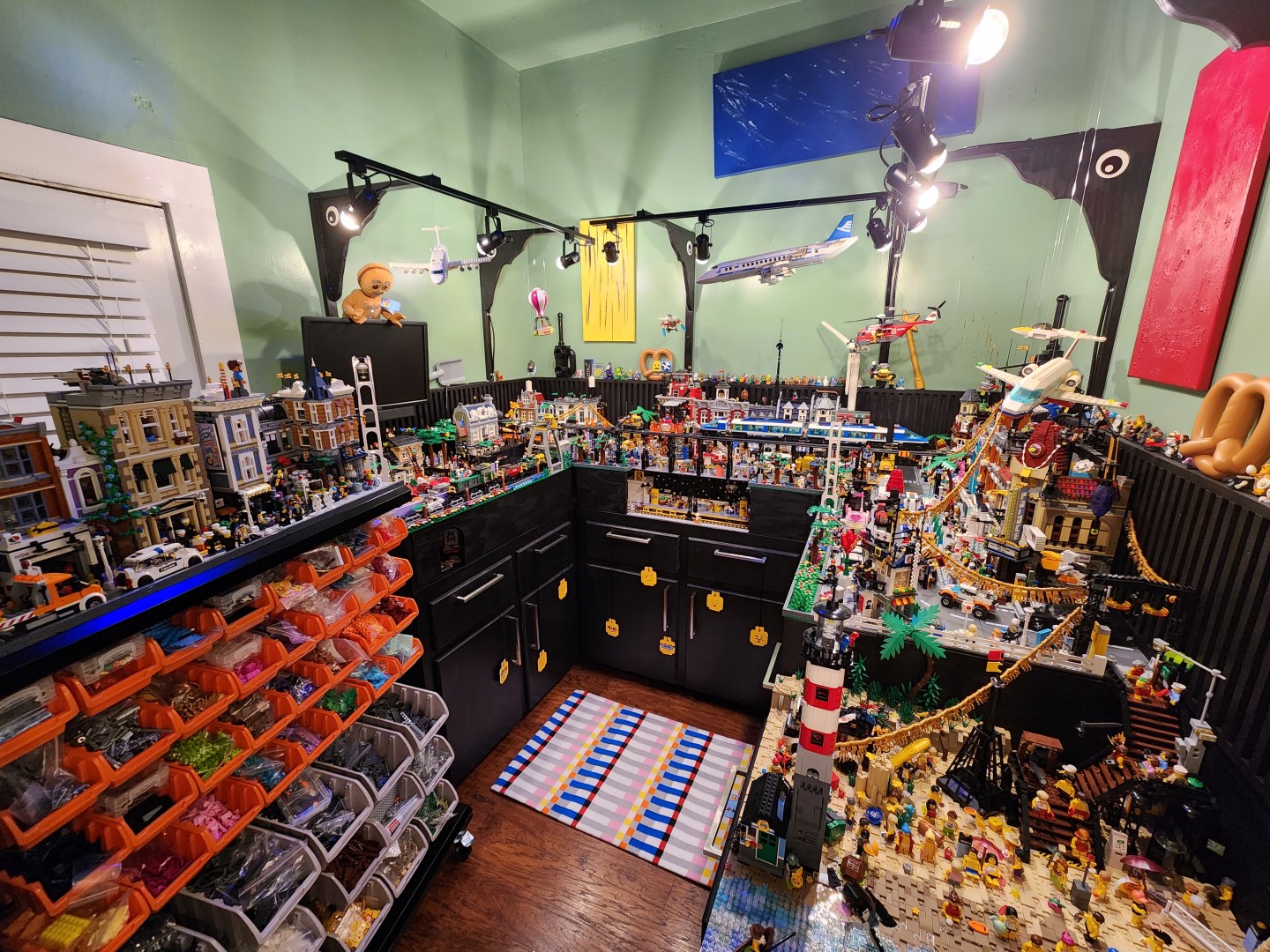 Wide view of the LEGO room with city builds, storage bins, lights, and display tables